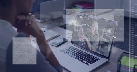 Man Watching Video Call on Laptop with Augmented HUD Overlays in Modern Coworking Space