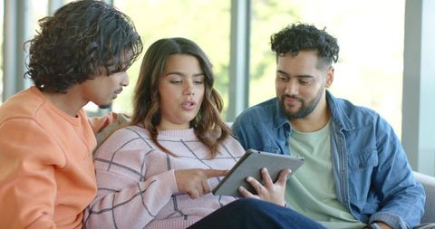 Young adults collaborating on tablet while relaxing on sofa in bright modern lounge