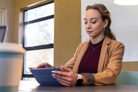 Focused professional woman using tablet in meeting room, wearing blazer and smartwatch