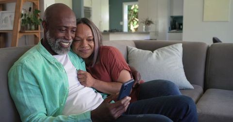 Mature couple cuddling on sofa sharing smartphone moment, cozy modern home lifestyle scene
