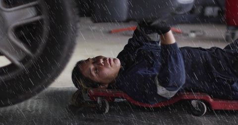Female mechanic lying on creeper inspecting vehicle undercarriage in garage