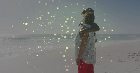 Couple embracing and watching ocean at sunlit beach with bokeh light overlay