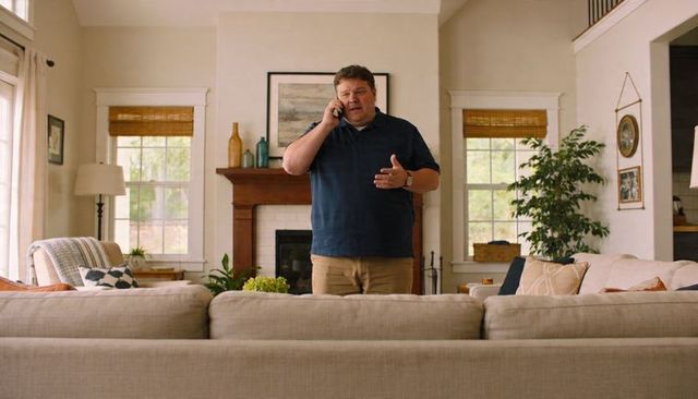 Man talking on smartphone in cozy contemporary living room behind sectional sofa