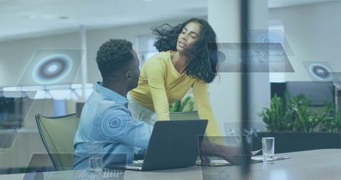 Collaborative team presenting data on laptop with futuristic holographic dashboard in office