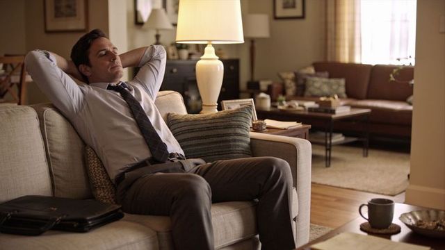 Businessman relaxing on sofa with loosened tie after work in cozy living room with briefcase