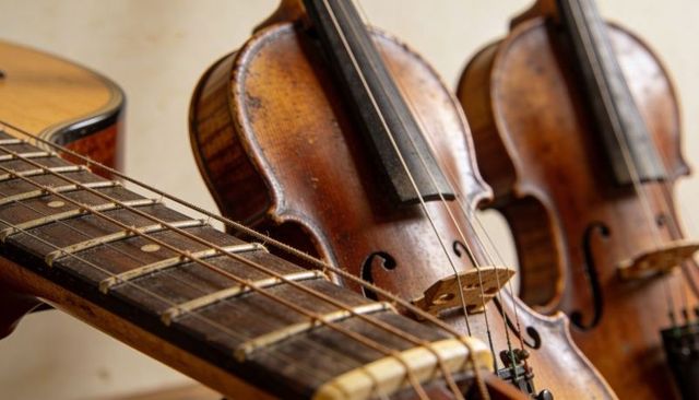 Worn acoustic guitar neck showing frets and strings with two vintage violins and patina