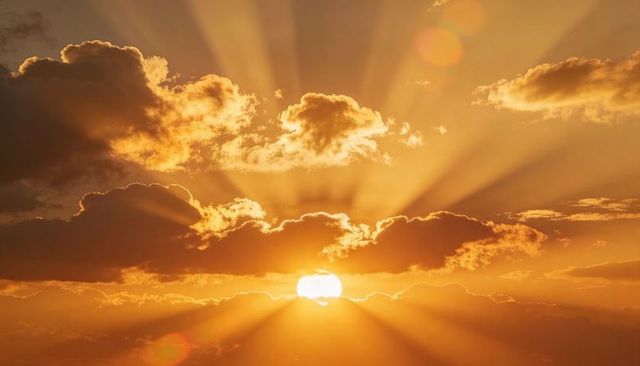 Golden sunrise radiating crepuscular rays through clouds over horizon with warm glow