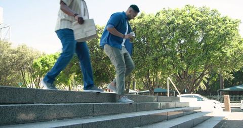 Diverse friends descending sunlit steps holding coffee and smartphone in casualwear