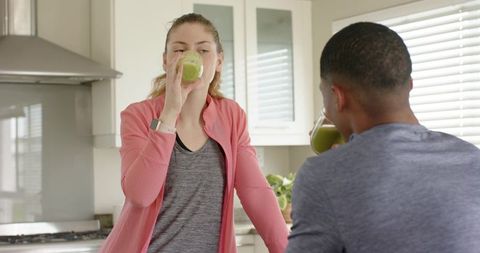 Healthy morning ritual: diverse couple drinking green smoothies in bright modern kitchen