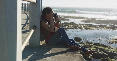 Woman photographing tidal pools from pier at coastline during low tide with DSLR camera
