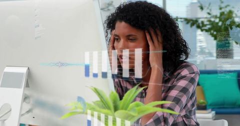 Woman holding head while analyzing data on desktop in home office with succulent plant