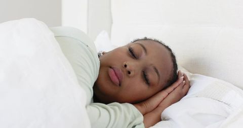 Mid-adult african american woman sleeping peacefully on white bed under soft duvet