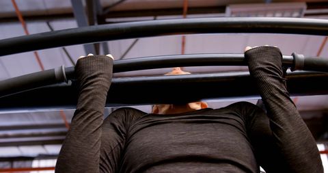 Caucasian woman determined achieving pull-up at gym