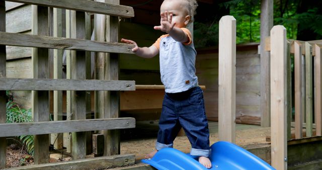 Cute toddler standing on blue slide outside wooden house - Download Free Stock Images Pikwizard.com
