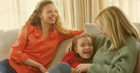 Multigenerational family laughing on sofa, mother daughter grandmother sharing cozy moment