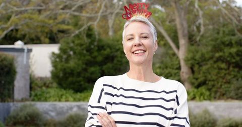 Joyful mature woman wearing merry christmas headband smiling outdoors in backyard portrait