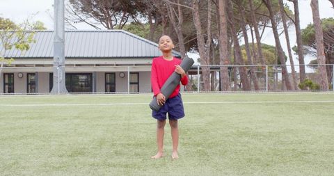 Young Boy Holding Yoga Mat on Grass Field in Casual Sportswear
