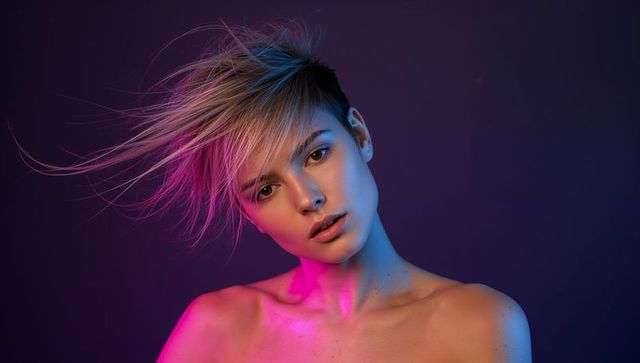 Windblown pixie haircut model in magenta and cyan lighting, earcuff, bare shoulders editorial