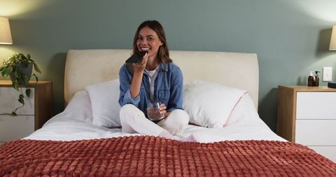 Woman relaxing in cozy bedroom with smartphone and drink
