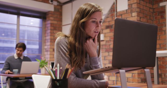 Caucasian businesswoman focusing on laptop in modern office while colleague working in the backgroun - Download Free Stock Images Pikwizard.com