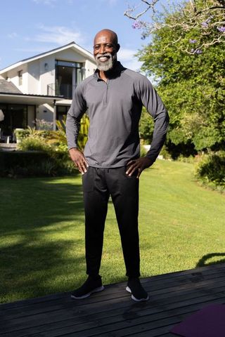 African american senior man standing and smiling on modern backyard deck wearing activewear