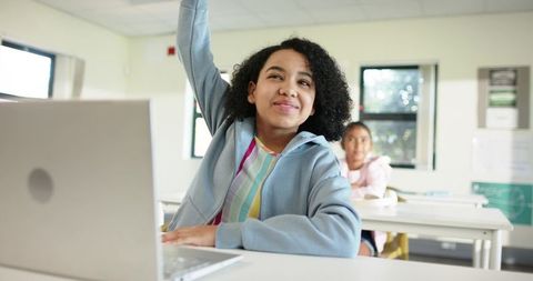 African American Teen Raising Hand in Classroom with Laptop Embracing Digital Learning