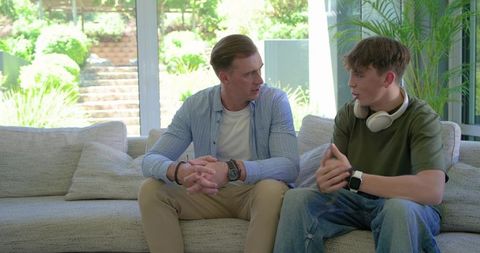 Mentor and teen discussing on couch in bright living room with headphones and garden view