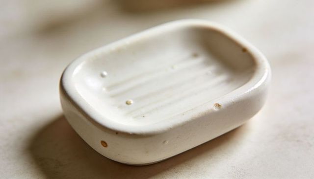 Off-white ceramic soap dish sitting on beige vanity showing water droplets and glaze chips