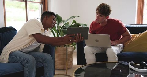 Young diverse friends collaborating on tablet and laptop in modern cozy living room