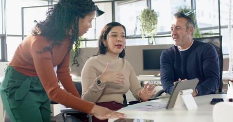Multicultural team collaborating around tablet and charts in sunlit modern office meeting