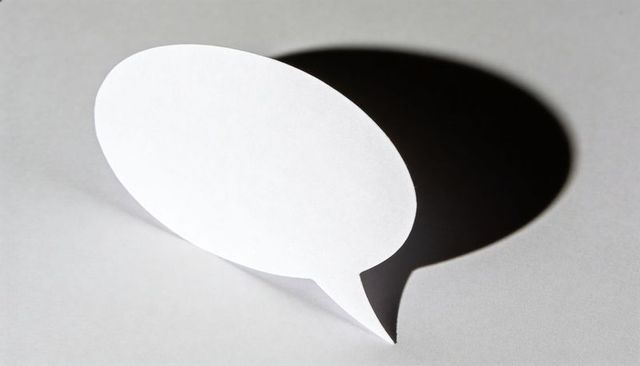 Paper speech bubble standing on gray tabletop casting bold shadow minimalist monochrome concept