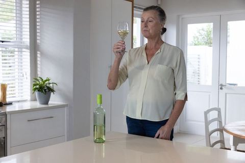 Senior Woman Analyzing White Wine in Modern Kitchen