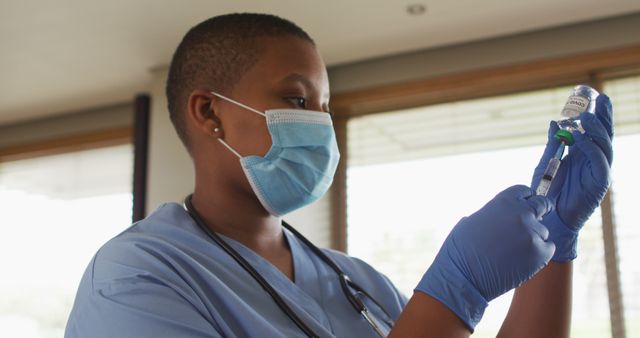 Healthcare worker wearing blue gloves and a protective mask is preparing a COVID-19 vaccine injection with a syringe. Ideal for use in health-related content, articles about vaccination, COVID-19 pandemic information, and educational materials about healthcare professionals. It highlights the importance of vaccinations and the efforts of frontline medical workers.