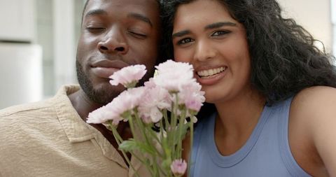 Smiling couple presenting pink chrysanthemum bouquet, intimate home portrait celebrating connection