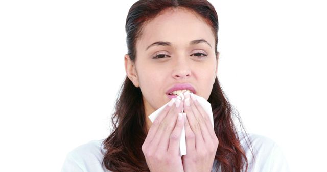 A young Caucasian woman is blowing her nose into a tissue, with copy space. Her expression suggests she might be dealing with a cold or allergies.