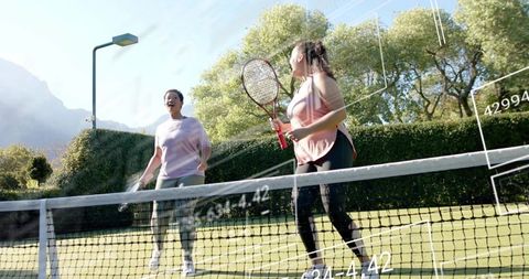 Two women playing tennis on sunlit grass court, casual fitness and friendship