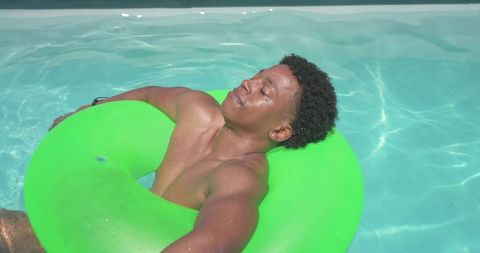 Relaxing african american young man floating on bright green inner tube in clear pool