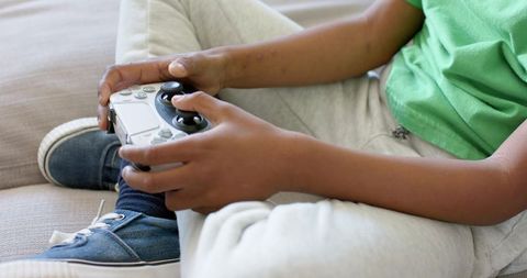 Young boy playing video game controller on couch wearing green shirt and sneakers