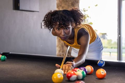 Woman aiming precision pool shot on black-felt table in bright modern lounge
