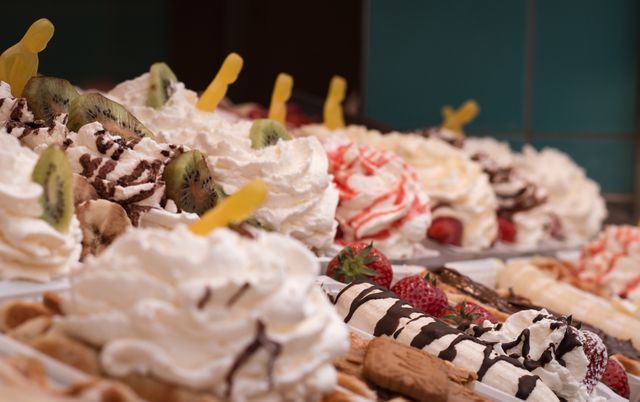Assortment of whipped cream desserts served with various toppings including kiwi and strawberries, drizzled with chocolate syrup. Perfect for use in advertisements for dessert shops, menus, or culinary blogs showcasing decadent sweet treats and snacks.
