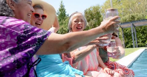 Joyful senior friends toasting by pool in relaxing atmosphere