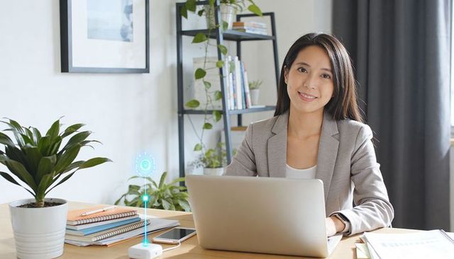 Asian woman working from home with laptop and holographic smart device, smiling professional