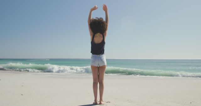 Back view biracial woman standing on beach and stretching hands up. Summer, free time, chill, vacation, happy time.