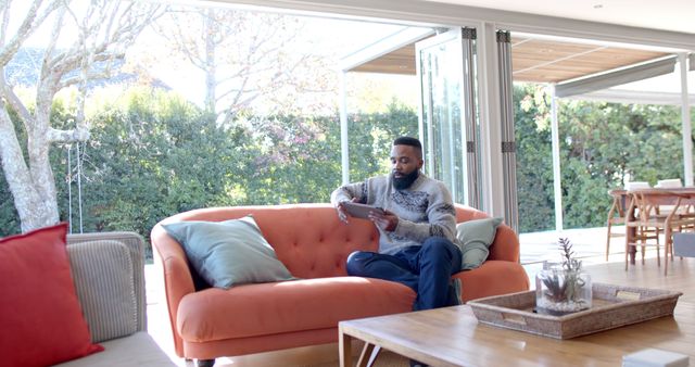 Man Relaxing with Tablet on Cozy Orange Sofa in Bright Living Room - Download Free Stock Images Pikwizard.com