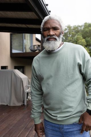 Senior african american man standing on deck checking wristwatch in sage sweatshirt