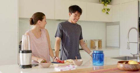 Couple cooking together in bright modern kitchen chopping tomatoes smiling while meal prepping