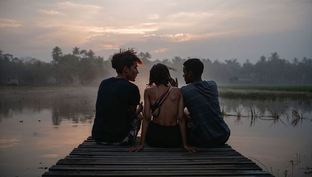 Teenagers sitting on wooden pier facing misty lake at sunset, relaxed summer evening
