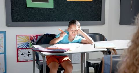 Focused biracial boy writing in sunlit classroom