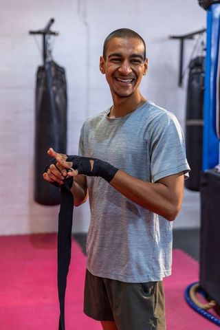 Young boxer wrapping hand wraps at boxing gym smiling and preparing for training