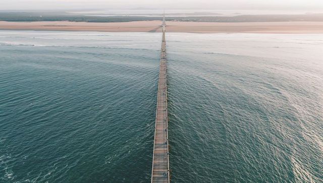Stretching wooden pier leading toward sandy beach minimalist aerial seascape people on jetty